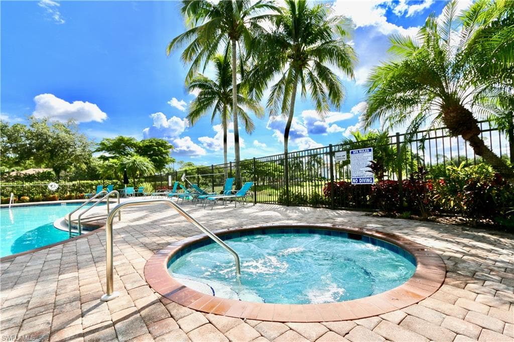 Expansive outdoor pool area featuring a circular spa with metal handrails, a curvilinear swimming pool, and paver decking