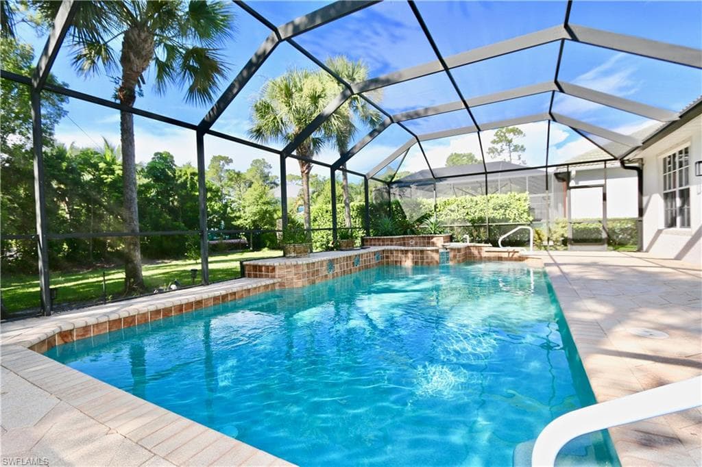 Screened outdoor pool area featuring a brick-tiled spa, a waterfall feature, and white handrails
