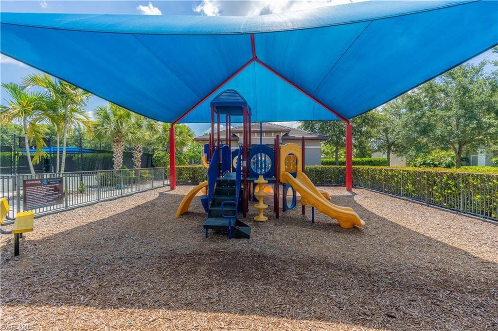 Community playground featuring a blue shade canopy, play structure with slides and climbing elements, and wood chip surfacing