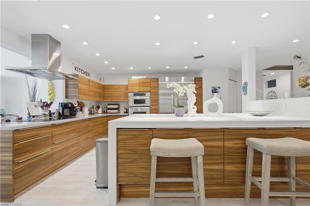 Contemporary kitchen featuring wood-finish cabinetry, white countertops, stainless steel appliances, a large center island with seating, and recessed lighting