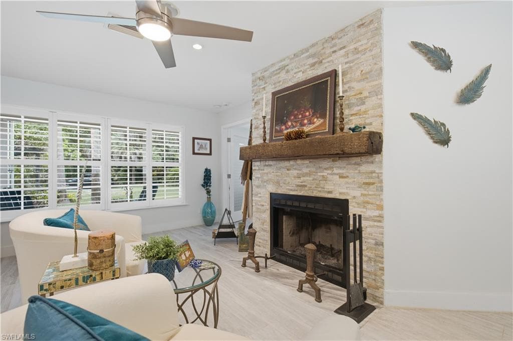 Living area featuring a stone-clad fireplace with a substantial timber mantelpiece, light wood-finish flooring, white plantation shutters, a ceiling fan with integrated lighting, and recessed lighting