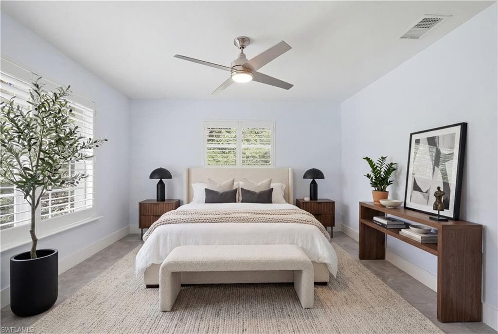 Spacious bedroom featuring light-toned walls, two windows with plantation shutters, a ceiling fan with integrated lighting, and light gray tile flooring