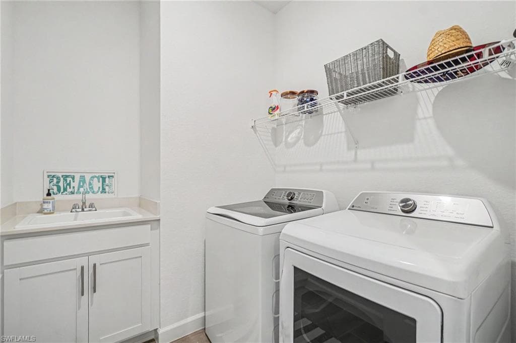 Dedicated laundry area featuring a utility sink with a light-toned countertop, white cabinetry with silver pulls, and an overhead wire shelving unit
