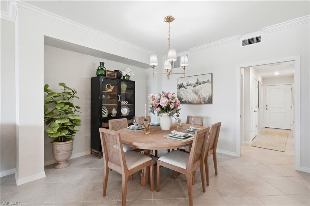 Dining area with a decorative chandelier, crown molding, and light-toned tile flooring