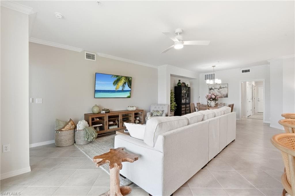 Spacious living area featuring light-toned tile flooring, crown molding, and a ceiling fan