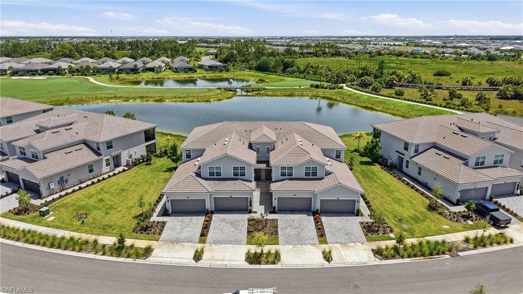 Modern townhome community featuring a large pond, expansive green spaces, paved driveways, and two-story residences with attached garages