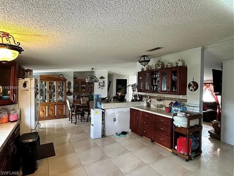 Kitchen area featuring ceramic tile flooring, a built-in kitchen peninsula, and dark wood-finish cabinetry with glass door accents