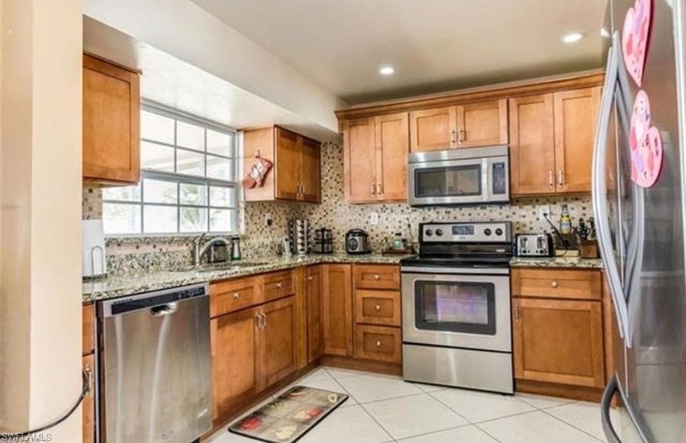 Kitchen featuring light wood cabinetry, stainless steel appliances, a window above the sink, granite countertops, and a tiled backsplash