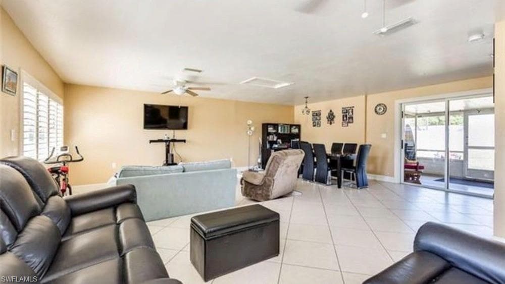 Open-concept living area featuring tile flooring, ceiling fans, and a sliding glass door providing access to an enclosed patio