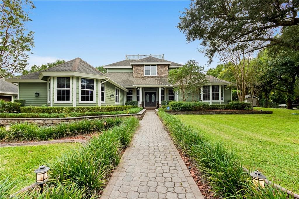 Exterior featuring light green siding, stone accents, multiple bay windows, and a paved walkway leading to the front entry