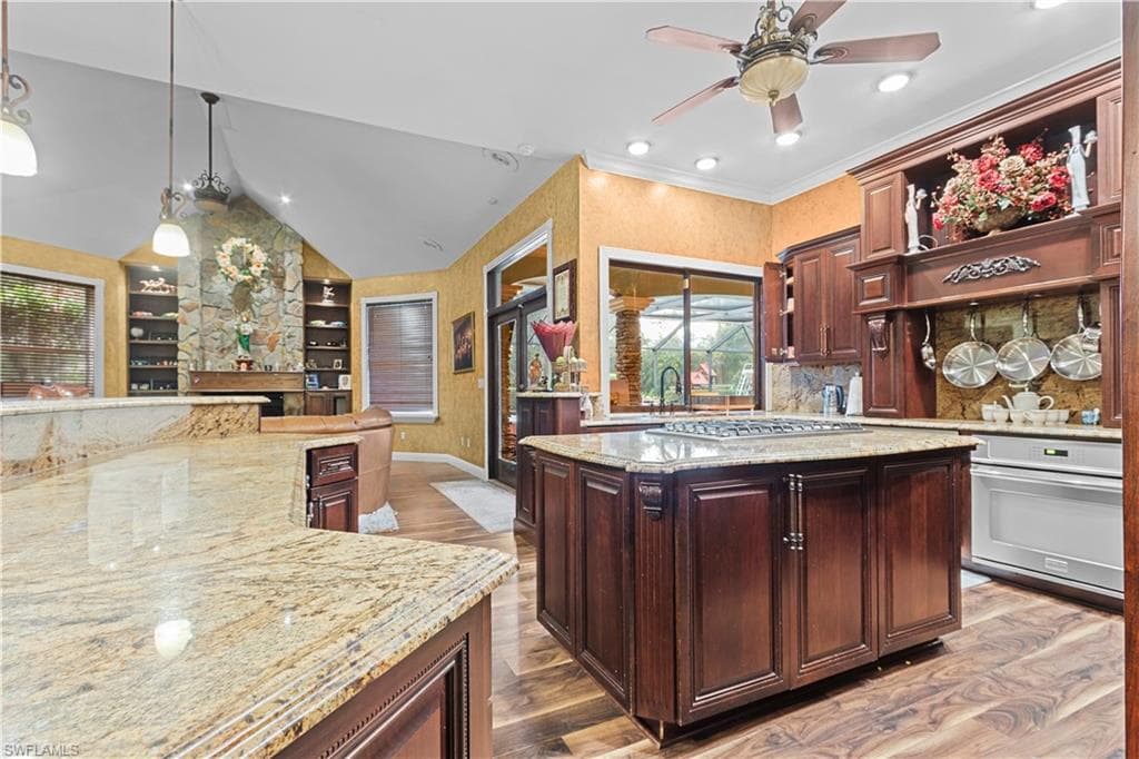 Kitchen featuring granite countertops, dark wood-finish cabinetry, a central island with a built-in cooktop, and wood-finish flooring