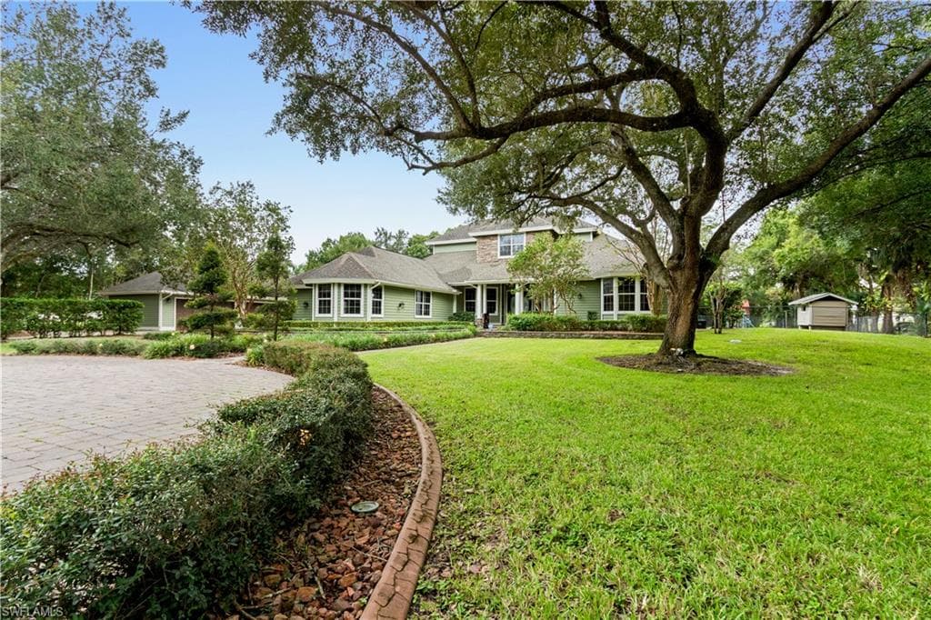 Expansive front yard featuring a large mature tree, a paved circular driveway, and a detached garage