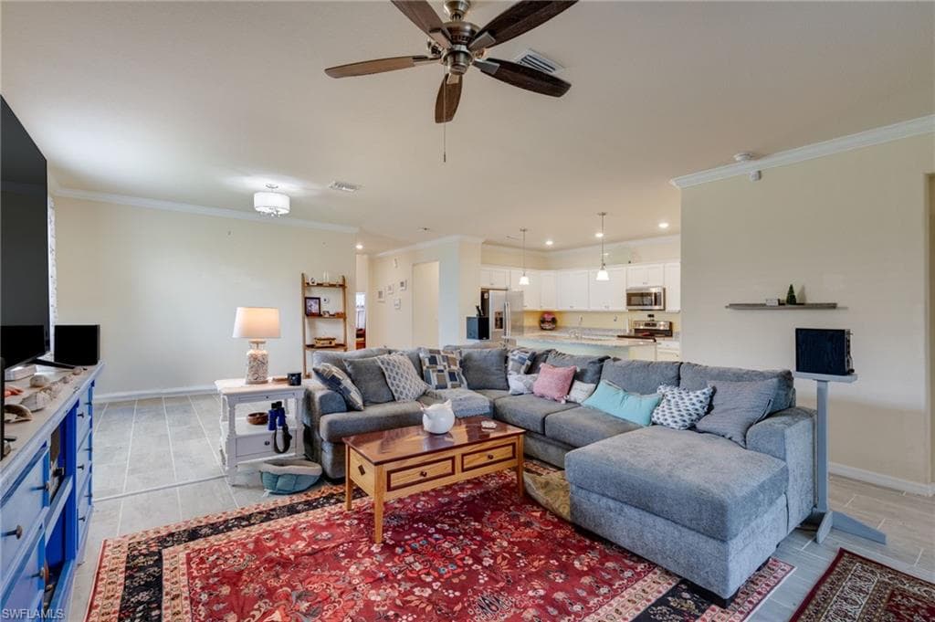 Open-concept living area featuring light-toned tile flooring, crown molding, and a ceiling fan with integrated lighting