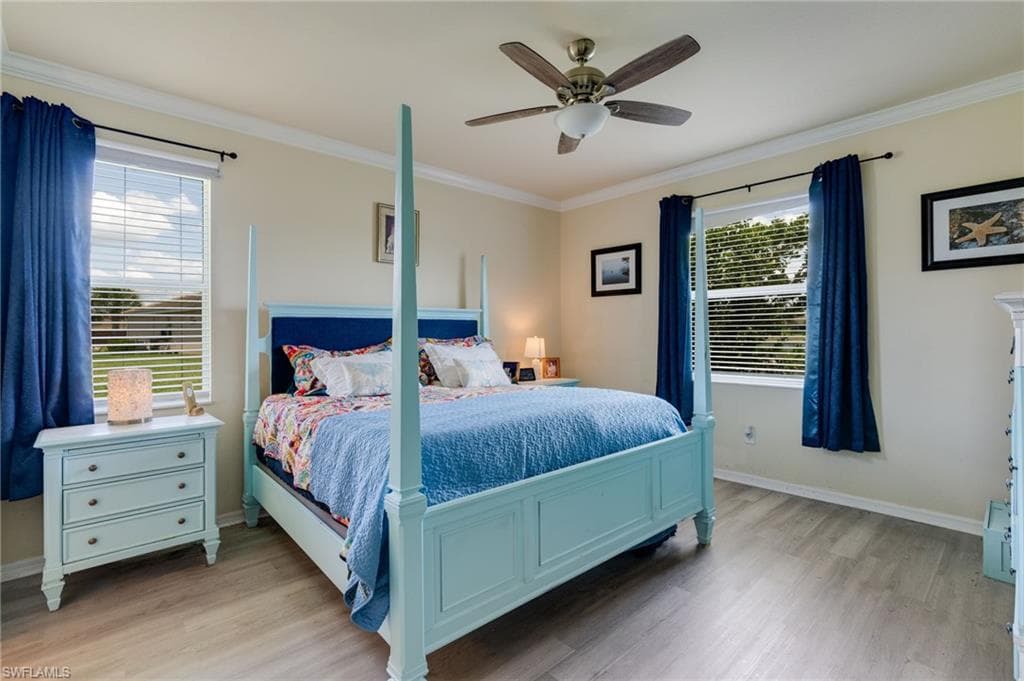 Bedroom featuring light wood-finish flooring, two large windows with blinds, a ceiling fan with light fixture, and crown molding