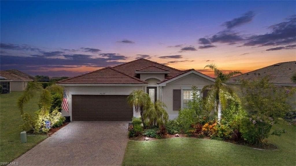 Single-story residence featuring a tile roof, an attached garage, a paver driveway, and mature landscaping with palm trees