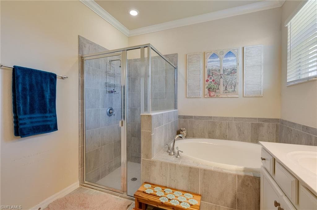 Bathroom featuring a glass-enclosed shower, a built-in soaking tub with tile surround, a single vanity with a white countertop, and crown molding
