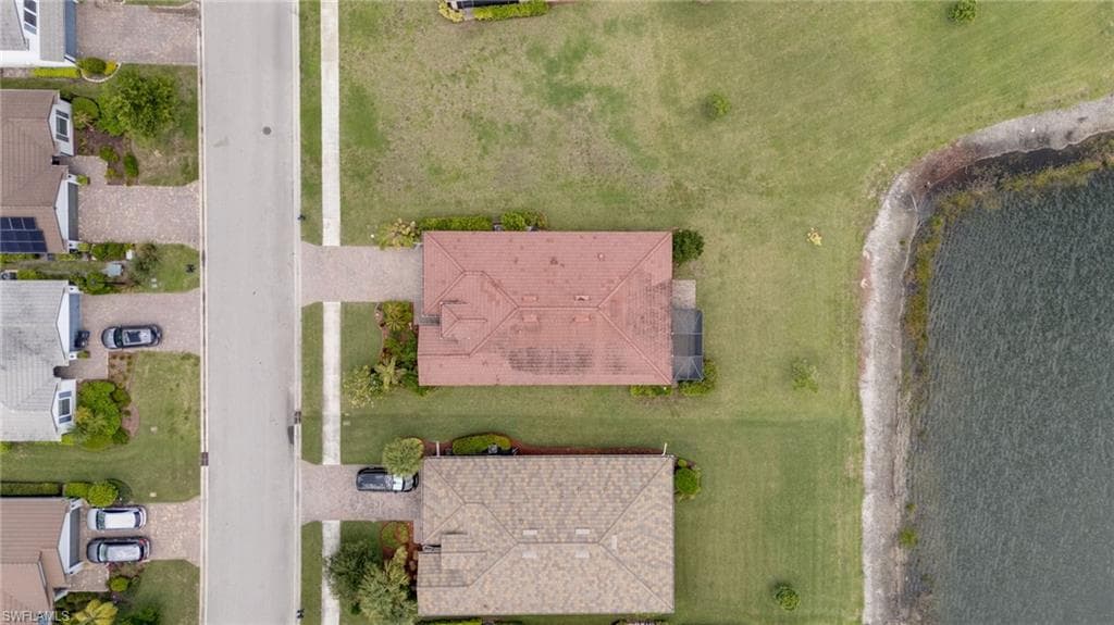 Property featuring a red tile roof, paved driveway, screened patio, and a grass lawn backing onto a body of water