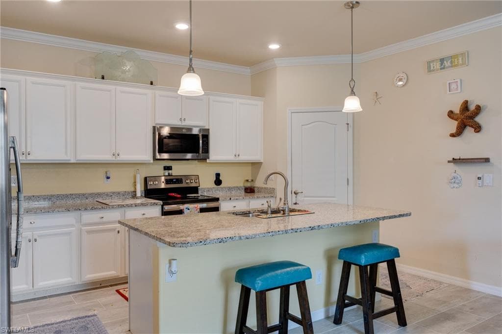 Kitchen featuring white cabinetry, stainless steel appliances, granite countertops, and an island with bar seating