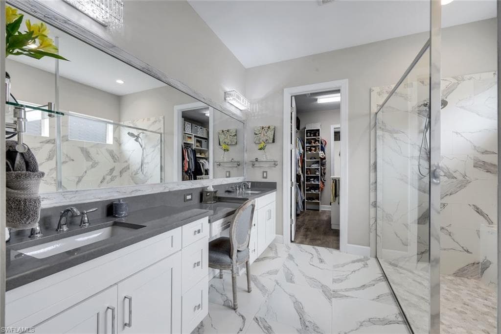 Spacious bathroom featuring marble-look tile flooring and shower surround, a double vanity with grey countertops, and a full-length mirror