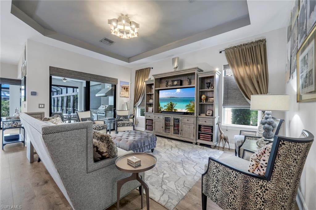 Spacious living area featuring tray ceilings, wood-finish flooring, and a large built-in entertainment center