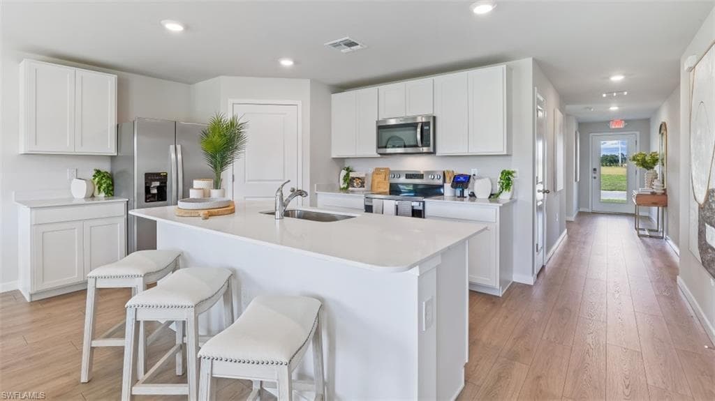 Model home. Kitchen with stainless steel appliances, white cabinetry, a breakfast bar, light wood-style floors, and recessed lighting