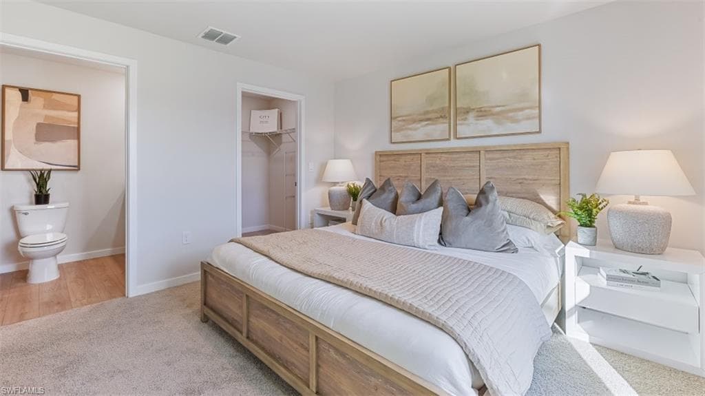 Model home. Bedroom featuring light carpet, a walk in closet, and ensuite bath