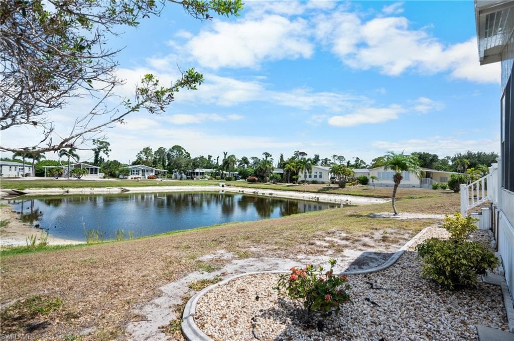 Waterfront property featuring a landscaped rock garden, mature palm trees, and a white exterior with a screened-in porch
