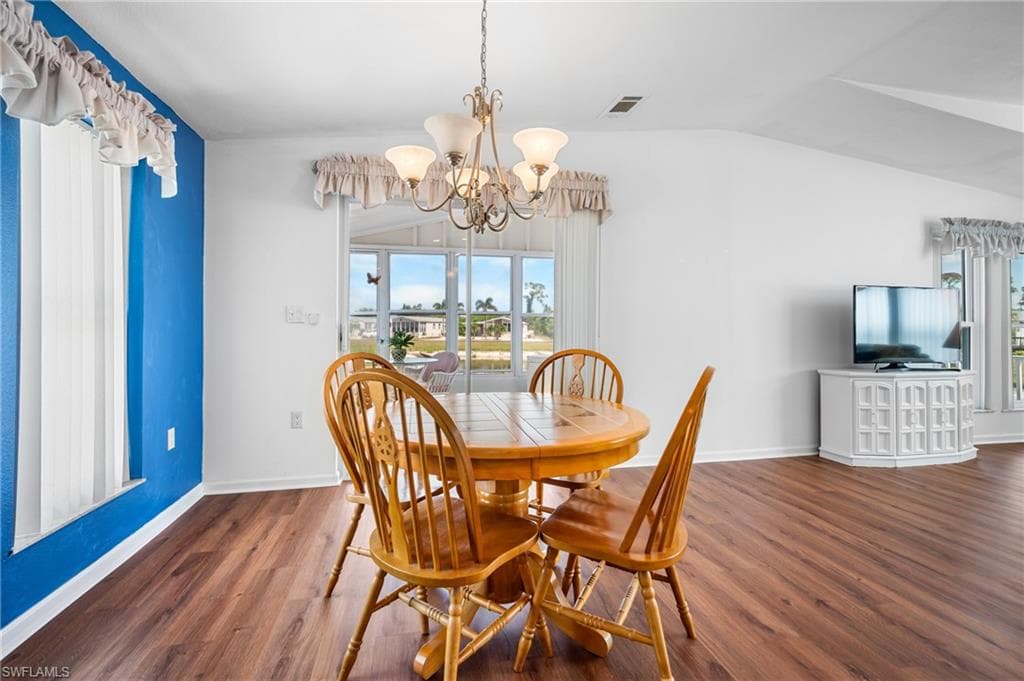 Interior space featuring wood-finish flooring, white walls with an accent wall, vaulted ceilings, and a chandelier lighting fixture