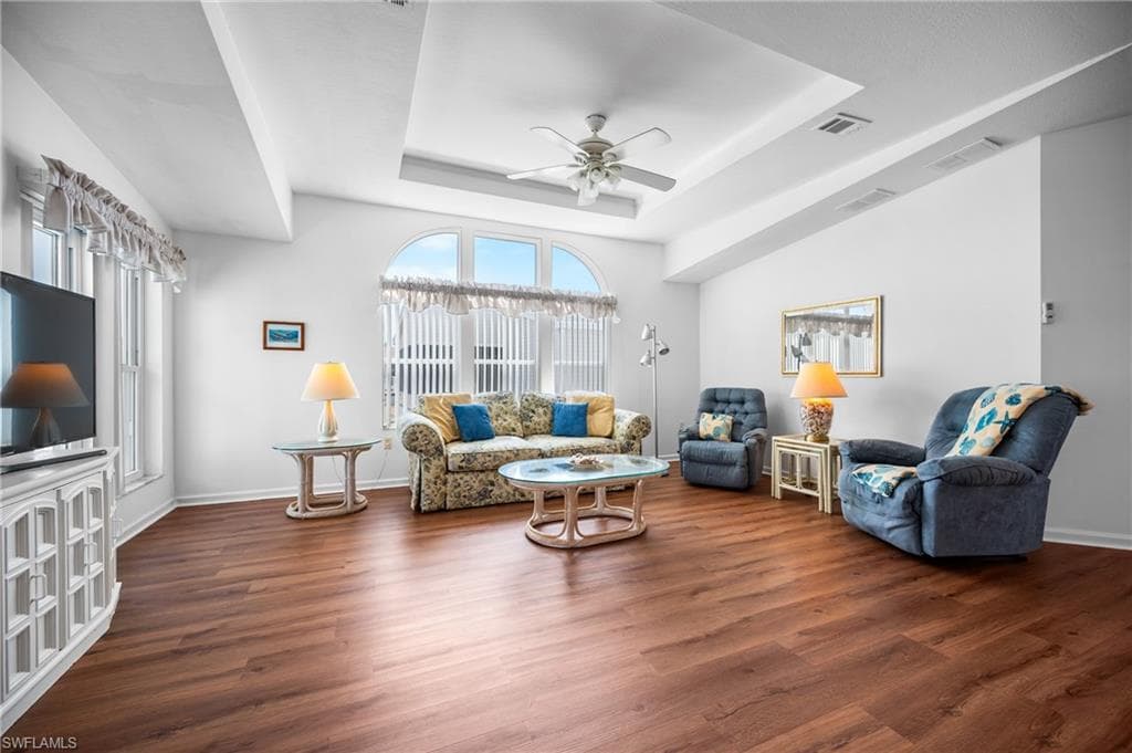 Spacious living area featuring rich wood-finish flooring, a tray ceiling, and an arched window