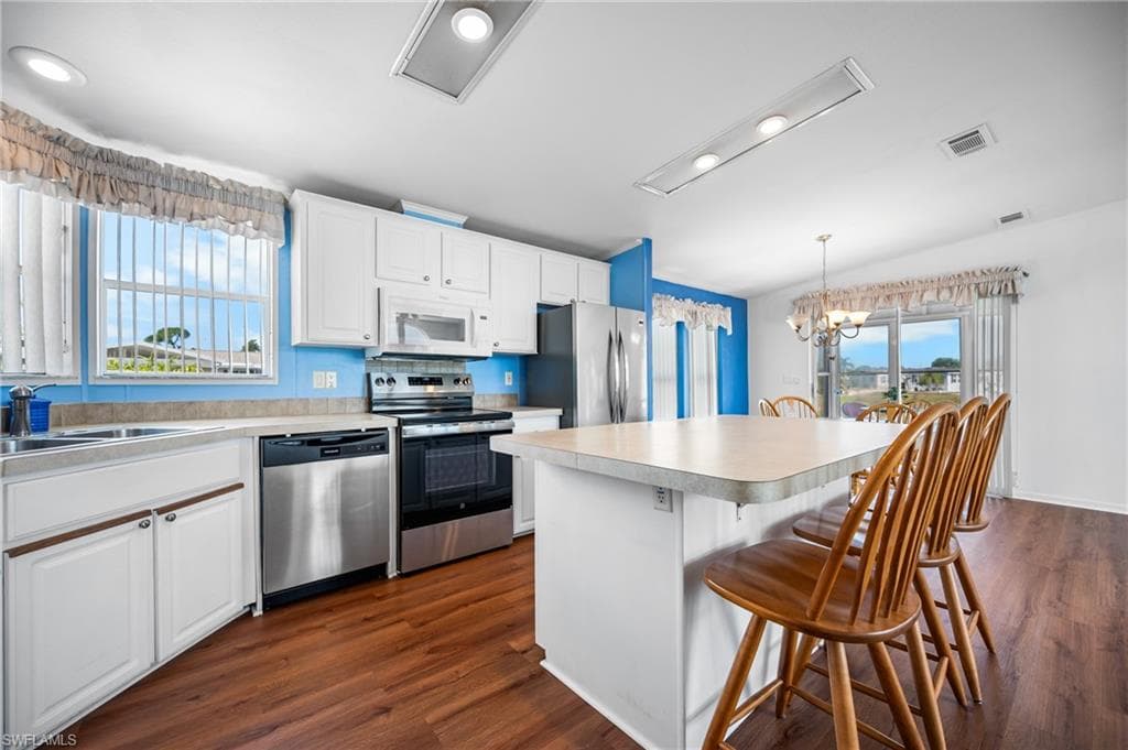 Kitchen featuring white cabinetry, stainless steel appliances, wood-finish flooring, a breakfast bar, and a sliding glass door