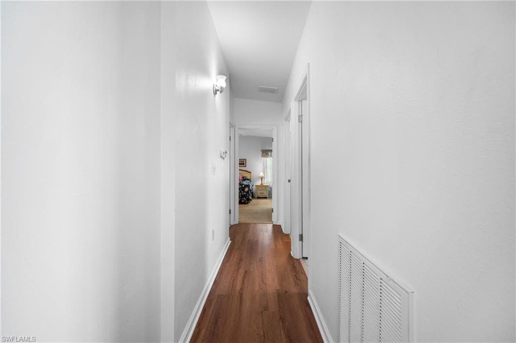 Hallway with wood-finish flooring, white walls, and wall-mounted light fixtures