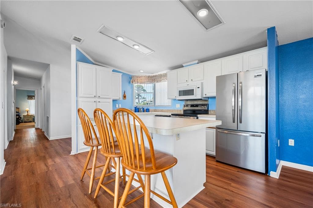 Kitchen featuring an island with breakfast bar seating, white cabinetry, and stainless steel appliances including a French door refrigerator, microwave, and range