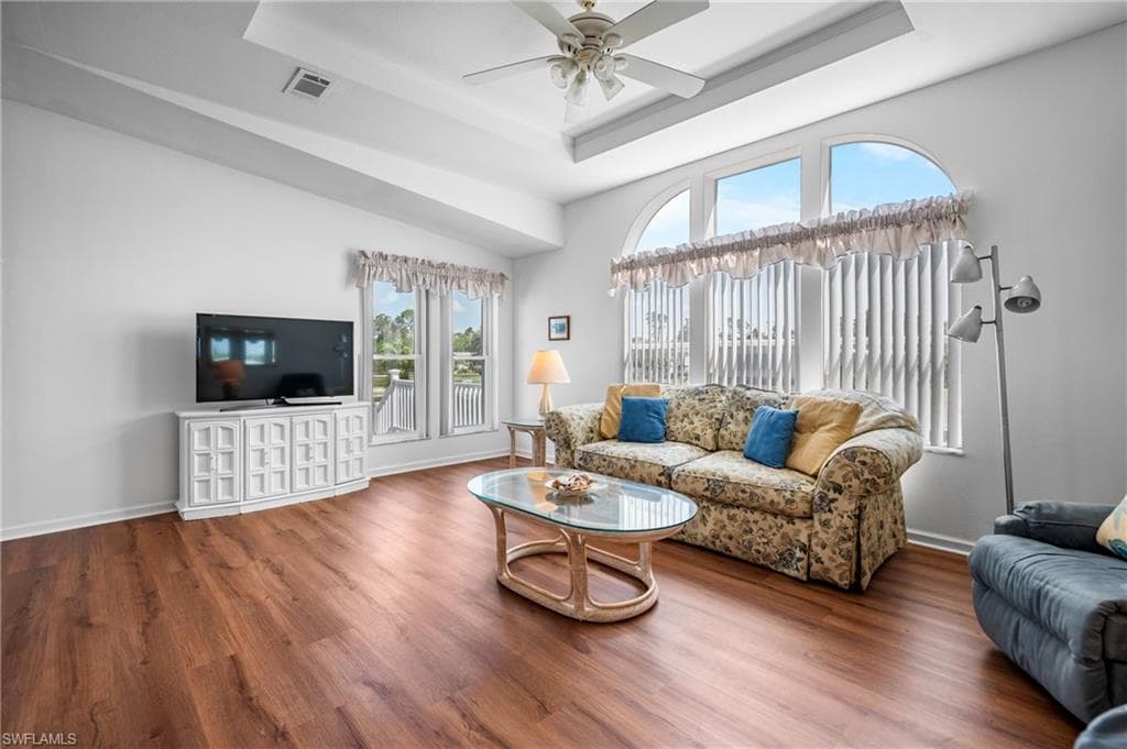 Spacious living area featuring wood-finish flooring, a tray ceiling, and a ceiling fan