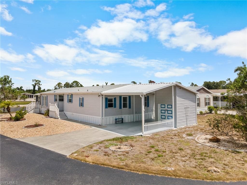 Light gray siding exterior with blue window shutters, white picket fence, and a covered carport
