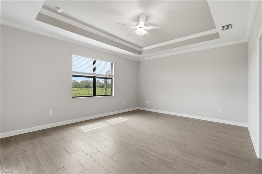 Spacious room featuring a tray ceiling, ceiling fan with integrated lighting, a large window with horizontal blinds, wood-finish flooring, and crown molding