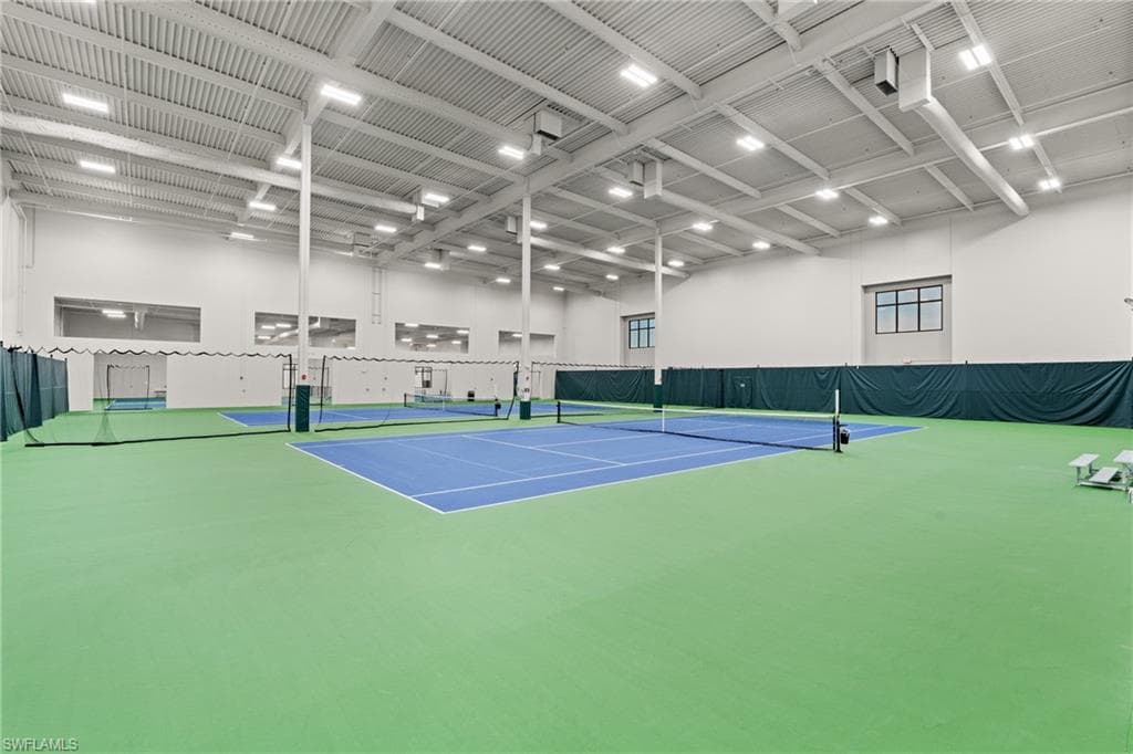 Indoor multi-court athletic facility featuring a light-colored corrugated ceiling, exposed structural beams, and bright overhead lighting