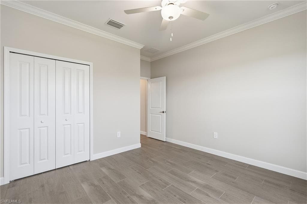 Spacious room featuring wood-finish flooring, light-toned walls, crown molding, and a ceiling fan with integrated lighting