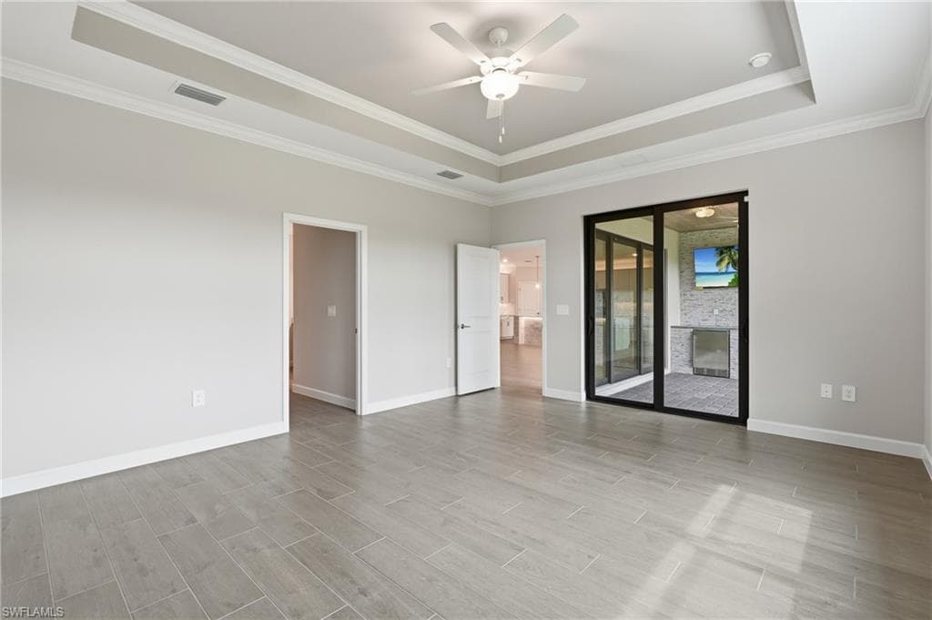 Spacious interior room featuring light wood-finish flooring, a tray ceiling with crown molding, and a ceiling fan