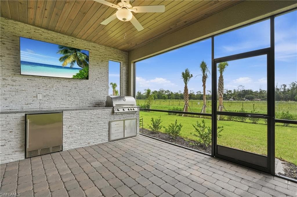 Screened outdoor living space featuring a built-in outdoor kitchen with stainless steel appliances, a ceiling fan, and wood-finish ceiling
