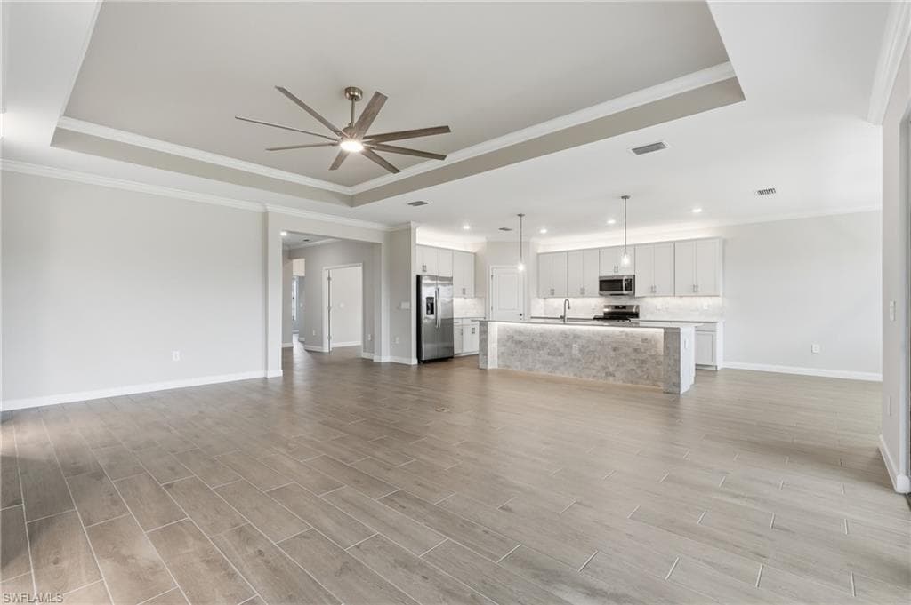Expansive open-concept living area featuring wood-finish flooring, a tray ceiling with a contemporary ceiling fan, and recessed lighting
