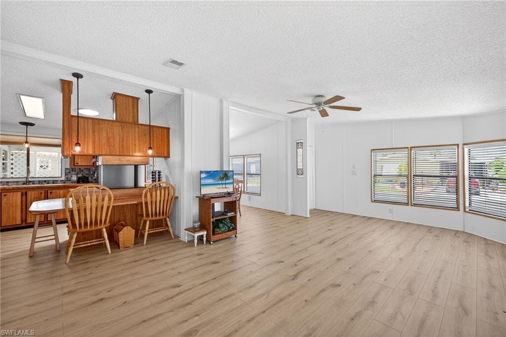 Open concept living area featuring wood-finish flooring, a ceiling fan, and multiple windows with blinds