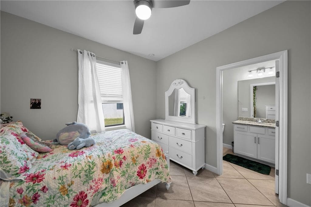 Bedroom with light tile patterned floors, baseboards, a sink, ceiling fan, and ensuite bathroom