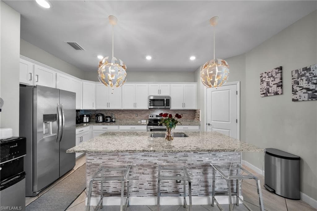 Kitchen featuring a breakfast bar area, decorative backsplash, appliances with stainless steel finishes, and an inviting chandelier