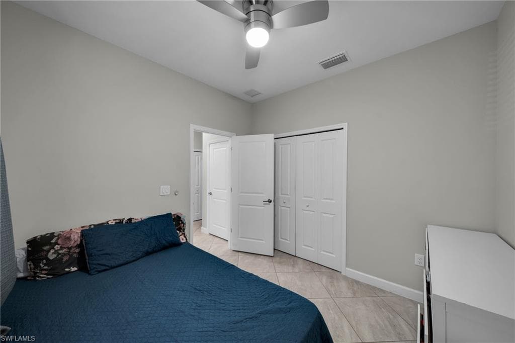 Bedroom featuring baseboards, light tile patterned flooring, visible vents, a ceiling fan, and a closet
