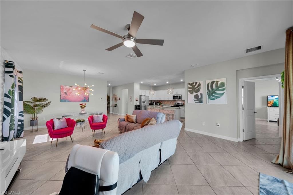 Living room with light tile patterned floors, ceiling fan with notable chandelier, baseboards, and visible vents