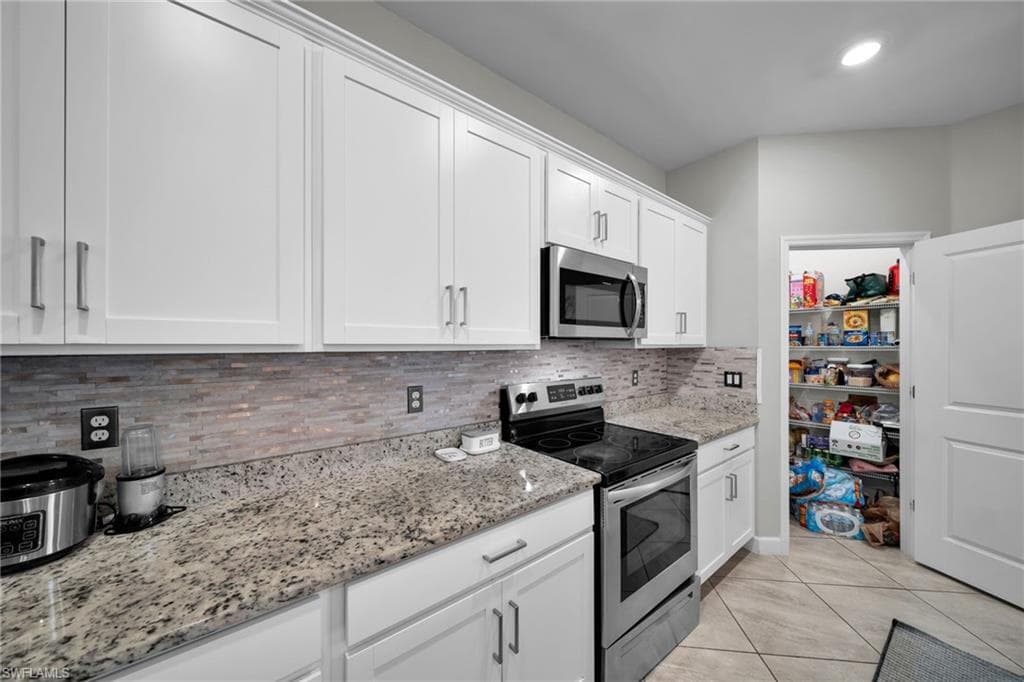 Kitchen featuring light tile patterned flooring, backsplash, light stone countertops, stainless steel appliances, and white cabinets