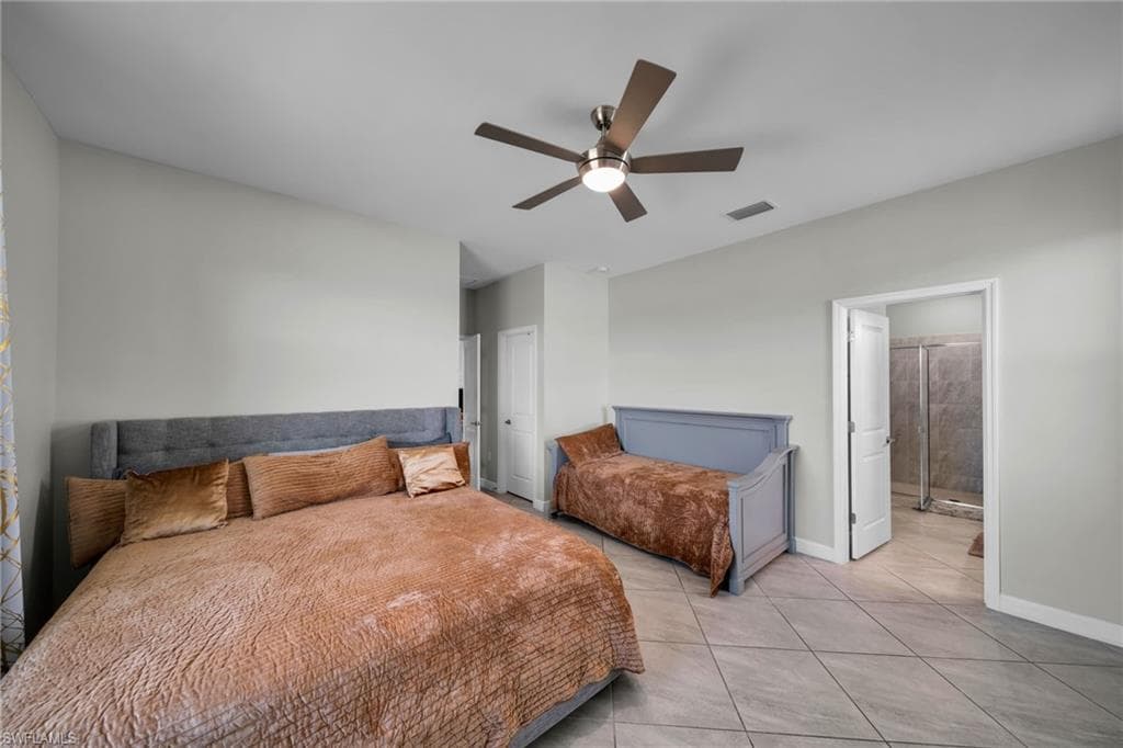 Bedroom with light tile patterned floors, baseboards, visible vents, a ceiling fan, and ensuite bathroom