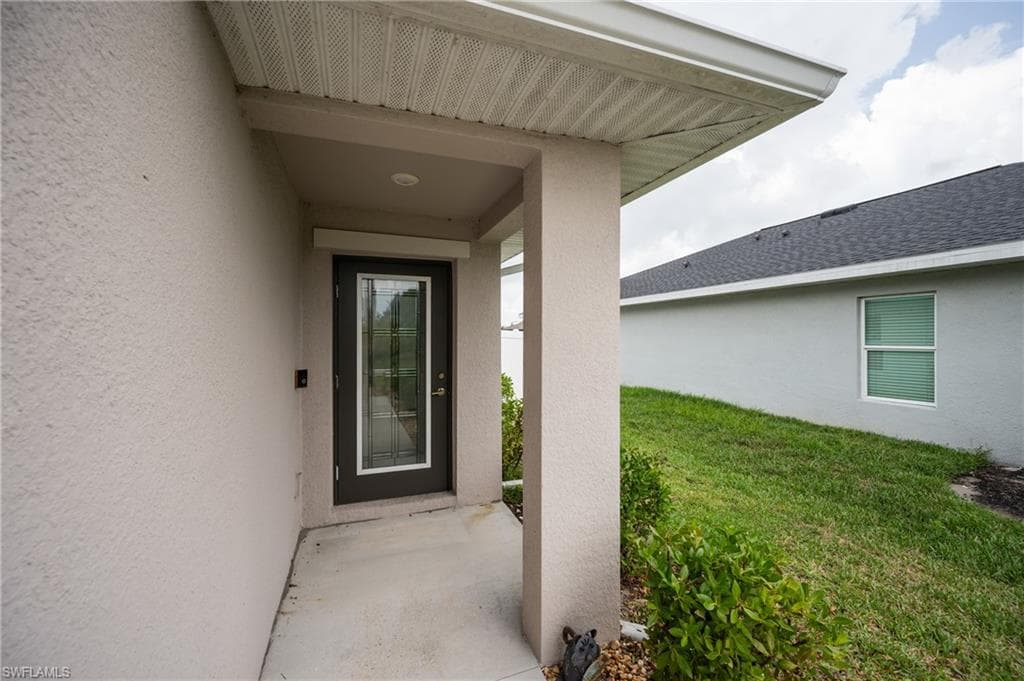 Covered entry with concrete flooring, stucco exterior, and a dark-framed entry door with decorative glass inserts