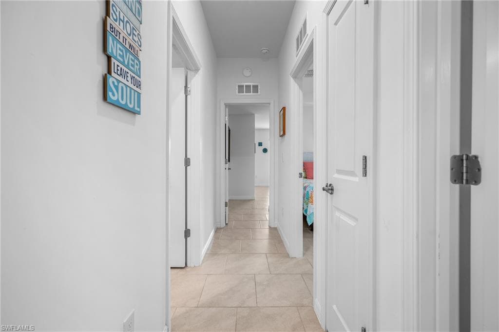 Hallway featuring tile flooring, white walls, and multiple white panel doors with brushed nickel hardware