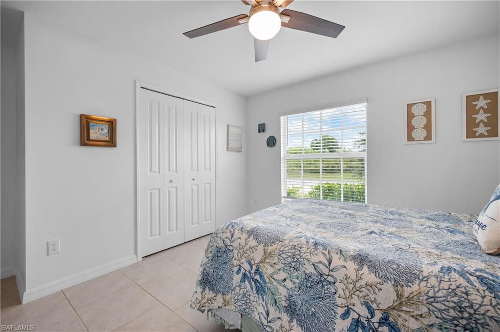 Bedroom featuring a window with horizontal blinds, a ceiling fan with light fixture, tile flooring, and a bi-fold closet